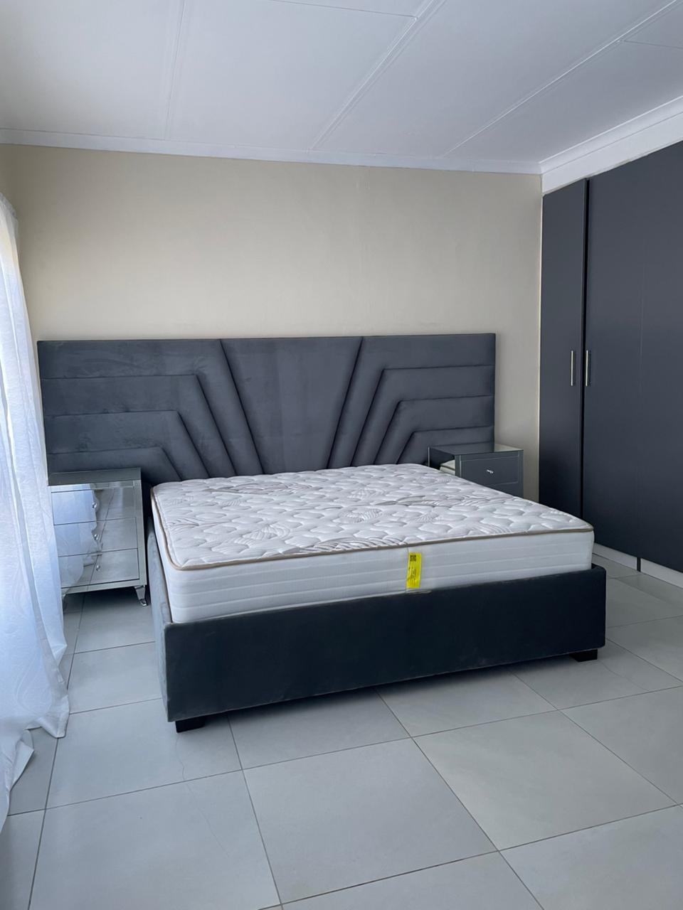 Bed with mattress and headboard in a room with tiled floor and white walls.
