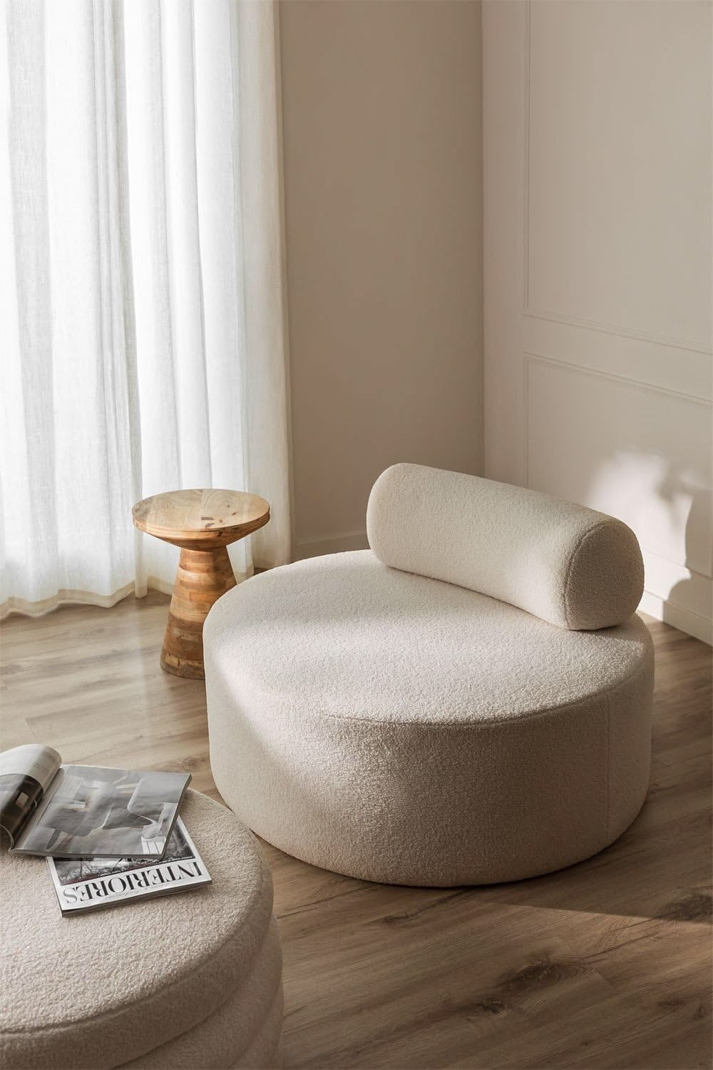 Cream bouclé Pebble round lounge chair with cylindrical bolster backrest in a sunlit room