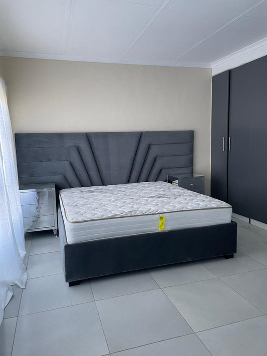 Bed with mattress and headboard in a room with tiled floor and white walls.